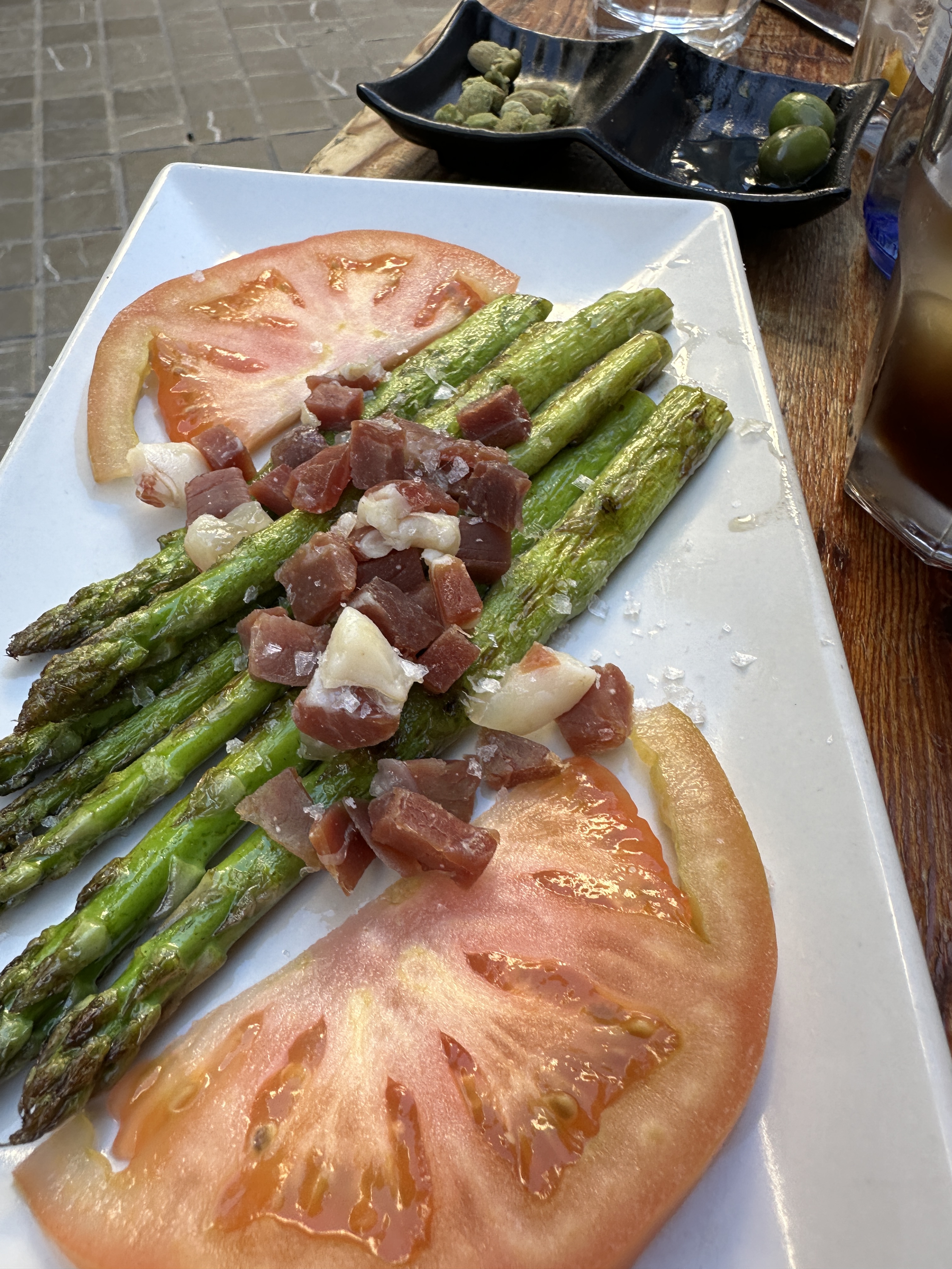 A simple dish of Asparagus centered between tomato slices and garnished with ham